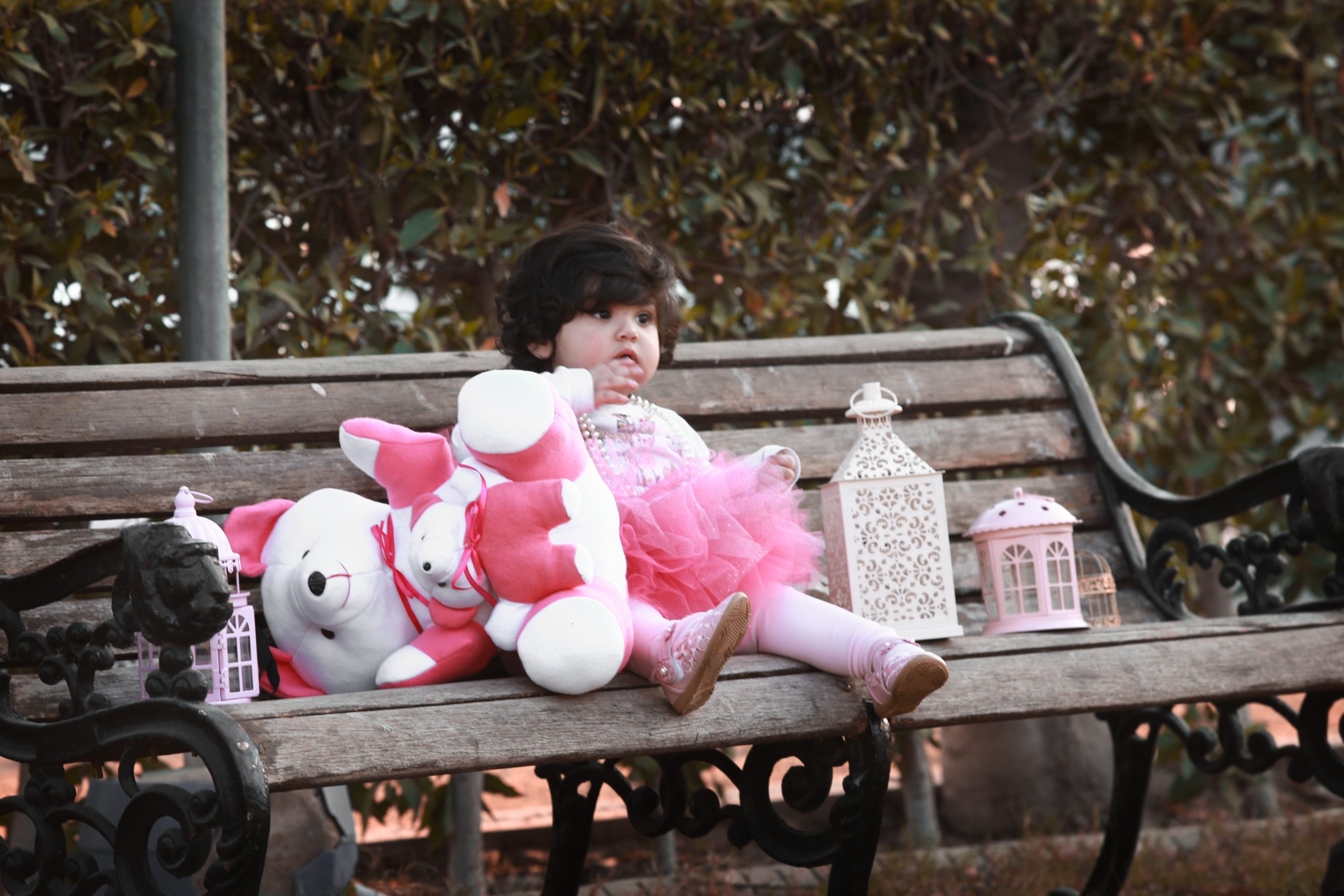 Cute One Year Little Baby Wearing Pink Fork Sitting on a bench at the park